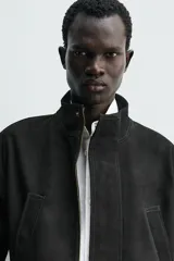 Parka de cuero color negro, de corte relajado, con cuello alto, cierre frontal con cremallera oculta y solapa con botones a presión. Cuenta con bolsillos frontales tipo cargo con solapa en la cadera y bolsillos de vivo en el pecho.