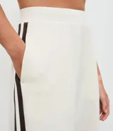 Pantalón deportivo de corte oversized estilo college, confeccionado en microfibra color crema con rayas laterales contrastantes en color marrón. Presenta cintura fija, bolsillos funcionales y frisos frontales.