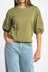 Remera de algodón color crudo con cuello redondo y mangas abullonadas de largo 3/4. Las mangas presentan detalles de encaje bordado y perforado con terminación elástica.