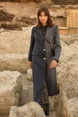 Tapado largo de sastrería con diseño bicolor, presentando un lado en tejido gris con textura y el otro en tejido gris con patrón de cuadros sutil. Cuenta con cierre frontal de botones de nácar, bolsillos con tapa y abertura trasera.