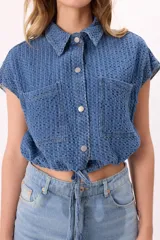 Camisa crop de denim texturado color celeste, con cuello camisero, mangas cortas, dos bolsillos frontales y lazo regulable en el ruedo.