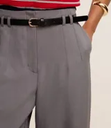 Pantalón de vestir gris de corte recto y cintura alta, con trabillas en la cintura, cierre tradicional y cinturón fino de material sintético con hebilla metalizada.