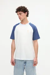 Remera estilo raglán color blanco en el cuerpo con mangas cortas color arena y cuello redondo marrón. Presenta un pequeño bordado en el pecho.