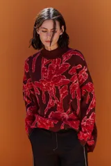 Buzo de tejido de punto con diseño floral en contraste, cuello redondo y mangas largas. Presenta una textura suave y un corte holgado.