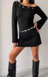 Vestido corto negro de manga larga, con diseño de escote asimétrico decorado con ojales metálicos en la parte superior. Presenta un corte ajustado y una cadena decorativa con dijes de estrellas en la cintura.