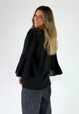 Blusa de algodón color gris oscuro con efecto gastado, mangas largas amplias con múltiples volados escalonados y terminaciones deshilachadas.