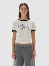 Remera de algodón con cuello redondo y mangas cortas con ribetes en contraste. Presenta un corte ajustado tipo baby tee y una estampa frontal con la frase 'Cry Baby'.