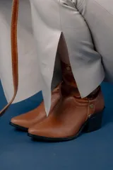 Bota corta estilo western de cuero color chocolate, con taco cuadrado y punta fina. Presenta detalle de correa con tachas metálicas y argolla en el tobillo.