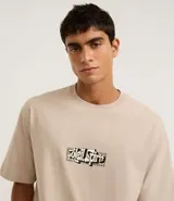 Remera de algodón color beige, corte relaxed (holgado), manga corta y cuello redondo. Presenta un pequeño estampado localizado con lettering estilizado en el pecho.