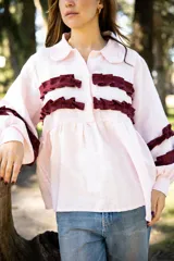 Camisa de lino color rosa claro con corte holgado, cuello camisero y mangas largas. Presenta detalles de volados horizontales en color bordó en el frente y en las mangas.