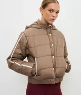 Campera puffer deportiva Get Over, color blanco con detalles de bies en color negro a lo largo de las mangas. Presenta cuello alto con capucha integrada, cierre frontal con botones a presión, bolsillos laterales con cremallera y puños con elásticos.