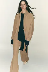 Chaqueta color tostado con cuello solapa, manga larga y cierre frontal con cremallera. Presenta bolsillos delanteros de plastrón con solapa y detalle de cintura ajustable con lazada.