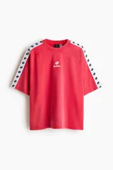 Remera de algodón oversized color rojo, con cuello redondo y mangas cortas raglán decoradas con una franja blanca lateral con logotipos negros de Lotto. Cuenta además con el logo de la marca estampado en el centro del pecho.