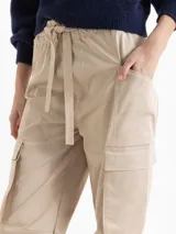 Pantalón cargo de corte recto y largo al tobillo, color beige. Presenta cintura elastizada con lazo ajustable, bolsillos laterales con tapa estilo utilitario y bolsillos adicionales en el delantero y la espalda.
