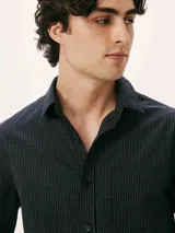 Camisa de manga larga con cuello clásico, cierre frontal de botones y bolsillo en el pecho. Presenta un diseño de rayas verticales finas en tonos azul y blanco.