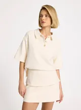 Chomba color crudo de tejido acanalado, corte holgado, cuello camisero, mangas cortas y anchas, bajo recto y caída estructurada.