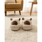 Pantuflas cerradas de peluche color beige con diseño de capibara, incluyendo orejas y nariz bordada. Cuentan con suela antideslizante.