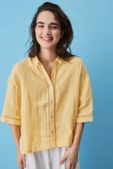 Camisa blanca de lino, con mangas anchas a tres cuartos, cuello clásico, cierre frontal con botones y detalles de calados verticales en la parte central y en los puños.