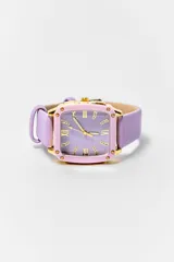 Reloj de pulsera con caja cuadrada dorada, bisel en tono rosado y esfera lila con números romanos y detalles de cristales. Cuenta con una correa de cuero sintético en color lila.