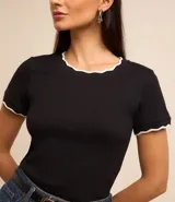 Blusa de algodón y elastano en color negro, de diseño entallado con cuello redondo y mangas cortas. Presenta terminaciones onduladas en color blanco contrastante en el cuello y los puños.