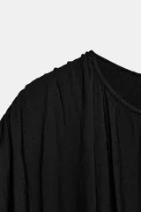 Top negro de punto con cuello redondo y manga corta estilo sisa. Presenta un diseño holgado en la parte superior con delicados frunces y detalle drapeado, y una sección inferior ajustada con frunces verticales y horizontales.