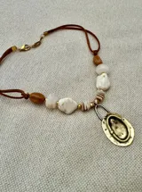 Collar con cordón de cuero marrón, cuentas de piedra blanca y marrón, y dije ovalado dorado.