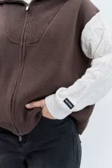 Cardigan de punto con diseño bicolor, cuerpo en color marrón y mangas largas en color crema con textura trenzada. Presenta cuello polo, cierre frontal con cremallera y puños acanalados.