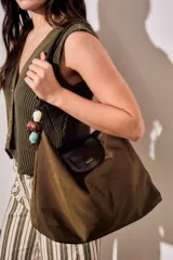 Cartera tipo shopper color marrón, con solapa frontal decorativa en tono más oscuro y tiras con nudos. Incluye herrajes dorados y un charm colgante con cuentas de madera.