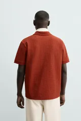 Polo de hombre color terracota con cuello solapa y cierre frontal de botonadura. Presenta un tejido texturizado tipo seersucker y un calce relajado.