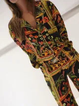 Conjunto de pijama de dos piezas con estampado floral y geométrico en tonos naranja, verde, amarillo y negro. Incluye camisa de manga larga con cuello y botones, y pantalón largo con cintura elástica.