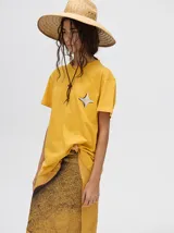Remera amarilla de ajuste holgado y corte cuadrado, con cuello redondo, mangas cortas y estampa de estrella de cuatro puntas en el pecho.
