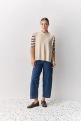 Chaleco tejido de punto color beige, con cuello redondo, terminaciones en rib y lazos laterales regulables que permiten ajustar la prenda.