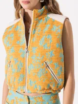 Chaleco corto color naranja con estampado de flores turquesa, cuello alto, cierre frontal y bolsillos con cierre.