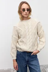 Sweater de tejido de punto grueso color crudo, con diseño de trenzas frontales, cuello redondo y mangas largas con puños ajustados.