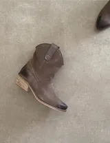 Bota corta estilo western de cuero color marrón, con taco cuadrado de 5 cm y diseño clásico. Presenta un acabado desgastado en la puntera y el talón.