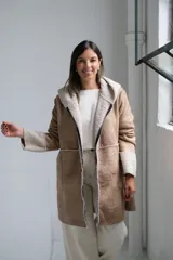 Tapado tipo gamuza con interior de corderito sintético, color beige con detalles en crudo. Presenta capucha, cierre frontal completo y puños con vuelta de corderito.