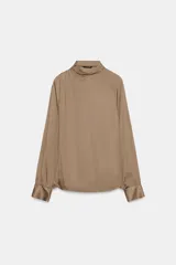 Blusa de tejido satinado color bordó, con cuello subido drapeado y manga larga con puños. Presenta detalle de pliegues frontales y cierre con botones laterales en el cuello.