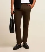 Pantalón de vestir color marrón, de corte slim y largo cropped. Confeccionado en tejido de algodón liso, con bolsillos laterales y traseros. Cierre frontal con botón y cremallera.