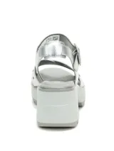 Sandalia plateada con tiras cruzadas y detalles de tachas, sujeción con hebilla al tobillo y plataforma con suela dentada.