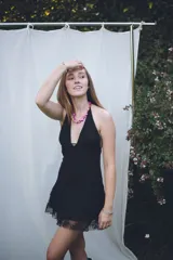 Vestido corto negro con escote en V profundo, estilo halter con tiras para atar al cuello. Presenta un diseño ajustado en el busto con tiras ajustables bajo el mismo que se cruzan y anudan en la espalda, y falda con volado en el ruedo con detalle de encaje.