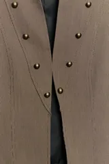 Blazer corto de estilo militar color tostado, con cuello redondo, manga larga y cierre frontal con ganchos metálicos. Presenta detalle de botones decorativos dorados en el frente y en los hombros, con costuras marcadas y forro interior a contraste.