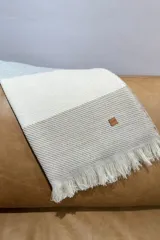 Pashmina de tejido liviano con diseño de bloques de color en tonos neutros, beige y crema, con terminación desflecada en los extremos y etiqueta de cuero sintético con logo grabado.
