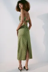 Vestido midi verde militar con estampado de lunares rosados, de corte recto y tirantes finos cruzados en la espalda. Presenta escote con frunces y detalle de lazo en el centro.