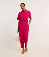 Camisa color fucsia de tejido airflow, con cuello camisero, mangas cortas con pliegues, cierre frontal con botones metalizados y bolsillos con solapa en el pecho.