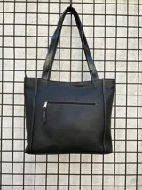 Cartera tipo tote de cuero vacuno negro con doble asa de hombro, panel superior liso y bolsillo exterior frontal con textura símil cocodrilo y costuras visibles en contraste.