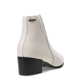 Bota tipo Chelsea de cuero color marfil, con paneles elásticos laterales, puntera redondeada y taco cuadrado bajo de color negro.