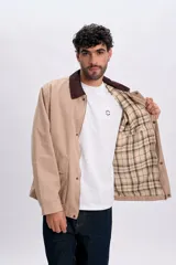 Campera color taupe de corte recto, con cuello camisero de pana marrón oscuro, cierre frontal oculto con botones a presión y grandes bolsillos frontales con solapa.