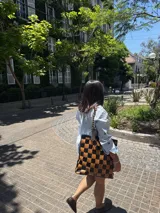 Bolso tipo tote de cuero trenzado a mano con diseño de damero en colores marrón y beige. Cuenta con doble asa trenzada y forro interior.