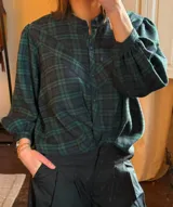 Camisa de franela a cuadros en tonos verde y azul marino, con cuello mao, cierre frontal de botones y mangas largas abullonadas con puños ajustados.
