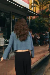 Chaqueta corta de cuello subido y manga larga, con diseño de cuadros en tonos azules. Presenta cierre frontal cruzado con botones oscuros y bolsillos de vivo en el delantero.